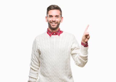 Kameraya bakarak yan el ve parmak ile işaret yüzünde kocaman bir gülümseme ile izole arka plan üzerinde kış kazak giyen genç yakışıklı adam.