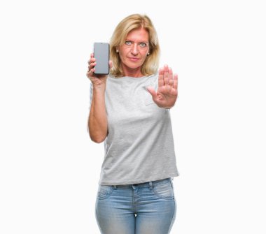 Orta yaş sarışın kadın boş ekran smartphone ile izole arka plan üzerinde gösterilen açık el dur işareti ile ciddi ve kendine güvenen ifade, savunma hareketi yapıyor