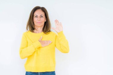 Üzerinde sarı kazak giyen güzel orta yaş kadın izole arka plan göğüs ve bir sadakat sözü yemin yapma avuç, el ile küfür