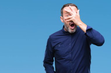 Mahcup ifadeyle parmaklarımın arasından görünen orta yaş ağarmış üst düzey adam yüz ve gözler el ile kapsayan şok bakmak izole arka plan üzerinde.