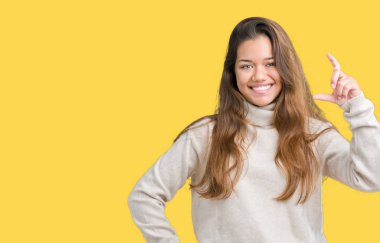 İzole arka plan gülümseyen ve süre seyir ve kamera boyutu işaret parmaklarıyla yapıyor el ile kendinden emin eller üzerinde boğazlı kazak giyen genç güzel esmer kadın. Ölçü kavramı.