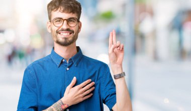 Young handsome man wearing glasses over isolated background Swearing with hand on chest and fingers, making a loyalty promise oath clipart