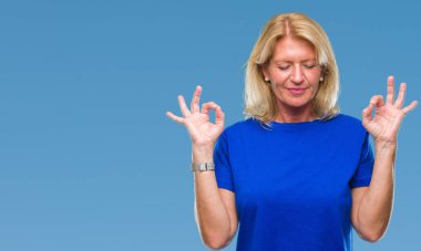 Orta yaş sarışın kadın izole arka plan üzerinde dinlenmek ve gülümseyen gözlerle parmak ile meditasyon jest yapıyor kapalı. Yoga kavramı.