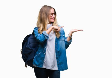 Hayret ve el ile sunulması ve parmak ile işaret ederken kameraya gülümseyen izole arka plan üzerinde kulaklık ve gözlük giyen genç güzel sarışın öğrenci kadın.