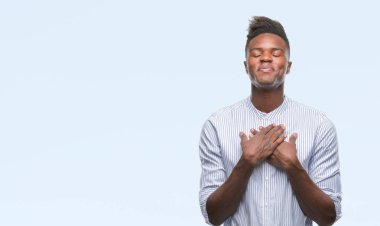 Göğüs kapalı gözler ve yüzünde minnettar jest ile genç Afro-Amerikan adam ile gülümseyen izole arka plan üzerinde eller. Sağlık kavramı.