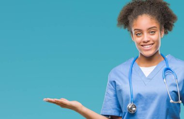 Genç afro Amerikalı doktor kadın neşeli sunulması ve kameraya bakarak avucunun ile işaret gülümseyen izole arka plan.