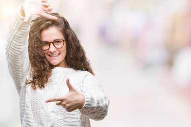 Güzel esmer kıvırcık saçlı Genç kız elle yapma çerçeve ve parmakları ile mutlu yüz gülümseyen izole arka plan üzerinde kış kazak giyiyor. Yaratıcılık ve Fotoğrafçılık kavramı.