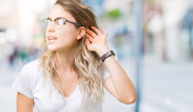 Gözlüklü bir işitme söylenti ya da dedikodu için dinleme kulak üzerinde el ile gülümseyen izole arka plan üzerinde güzel sarışın genç kadın. Sağırlık kavramı.