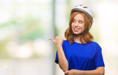 Seyir ve başparmak yanında yukarıyı mutlu yüz ile gülümseyen izole arka plan üzerinde bisikletçi kask giyen genç güzel kadın.