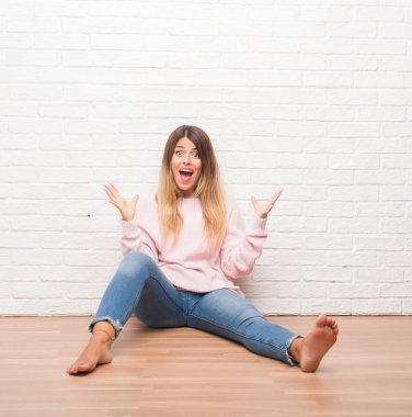 Yerdeki beyaz tuğla üzerinde oturan genç yetişkin kadın çılgın ve başarı için hayran kaldırdı kollarını açarak kutlama duvar ve heyecanlı çığlık gözleri açık. Kazanan kavramı