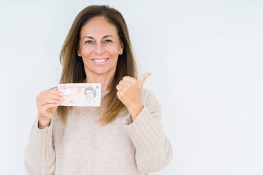 10 pound banknot işaret ve başparmak kadar mutlu yüz gülümseyen tarafı ile gösteren izole arka plan üzerinde tutan orta yaş kadın
