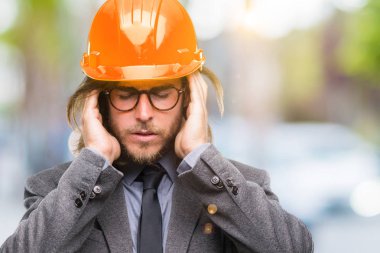 Çünkü üzerinde güvenlik kask giymiş uzun saçlı Genç yakışıklı architec adam arka plan baş baş ağrısı için el ile izole stres. Migren muzdarip.