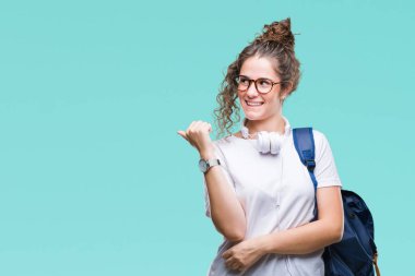 Sırt çantası ve kulaklıklar arıyorsunuz ve başparmak yanında yukarıyı mutlu yüz ile gülümseyen izole arka plan üzerinde giyen genç esmer öğrenci kız.