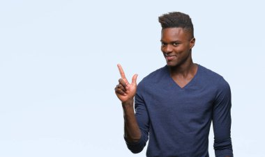 Kameraya bakarak yan el ve parmak ile işaret eden genç Afro-Amerikan adam yüzünde kocaman bir gülümseme ile izole arka plan üzerinde.
