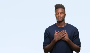 Göğüs kapalı gözler ve yüzünde minnettar jest ile genç Afro-Amerikan adam ile gülümseyen izole arka plan üzerinde eller. Sağlık kavramı.