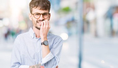 Genç yakışıklı adam stresli ve gergin ile izole arka plan üzerinde gözlük takan tırnak ısırma dudaklarından eller. Anksiyete sorunu.