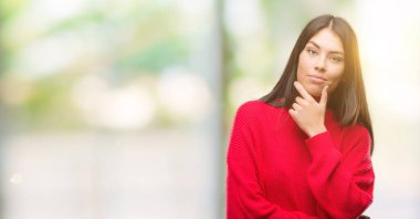 Genç güzel İspanyol emin çapraz kollar ve çeneme kaldırdı el ile gülümseme ile kameraya bakarak kırmızı kazak giyiyor. Pozitif düşünce.