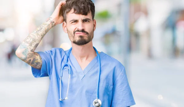 Young handsome nurse man wearing surgeon uniform over isolated background confuse and wonder about question. Uncertain with doubt, thinking with hand on head. Pensive concept.
