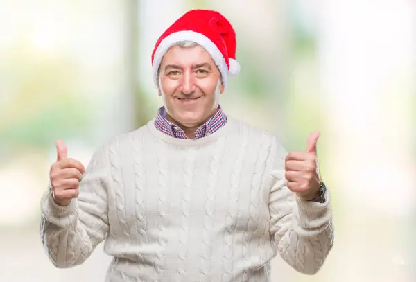 ハンサムな年配の男性の手で肯定的なジェスチャーを行う分離背景成功記号の上クリスマス帽子をかぶっている親指を笑顔と幸せを 勝者ジェスチャー晴れやかな表情でカメラを見てください — ストック写真