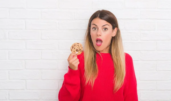 白いレンガ壁食べるチョコレート以上若い成人女性チップ クッキー驚き顔 恐怖表現と興奮とショックで怖い — ストック写真