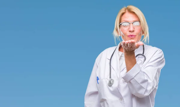 Middle age blonde doctor woman over isolated background looking at the camera blowing a kiss with hand on air being lovely and sexy. Love expression.