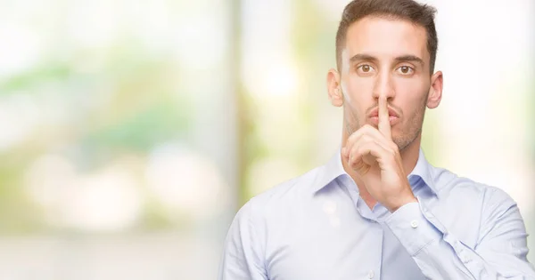 Handsome young businessman asking to be quiet with finger on lips. Silence and secret concept.