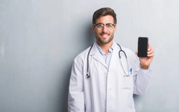 Handsome Young Doctor Man Grey Grunge Wall Holding Smartphone Happy — Stock Photo, Image