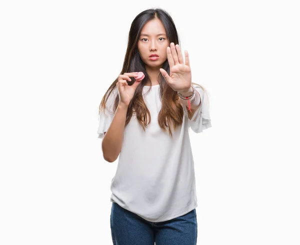 年轻的亚洲妇女吃粉红色的 Macaron 甜过孤立的背景与张开手做停止标志认真和自信的表达 防御姿态 — 图库照片