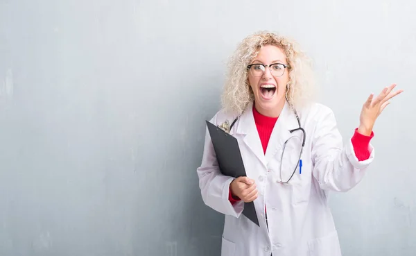 Junge Blonde Ärztin Über Grunge Graue Wand Mit Klemmbrett Sehr — Stockfoto