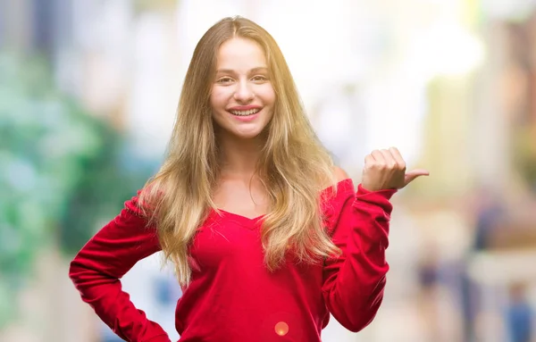 探していると親指側に上向きの幸せそうな顔を浮かべて孤立の背景に赤いセーターを着ている若い美しいブロンドの女性 — ストック写真