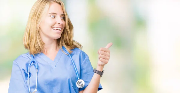 美丽的年轻医生妇女穿着医疗制服在孤立的背景看着骄傲 微笑着做大拇指做手势的身边 — 图库照片