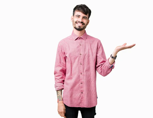 年轻英俊的男人穿着粉红色的衬衫在孤立的背景微笑着欢快的呈现和手掌看着镜头 — 图库照片