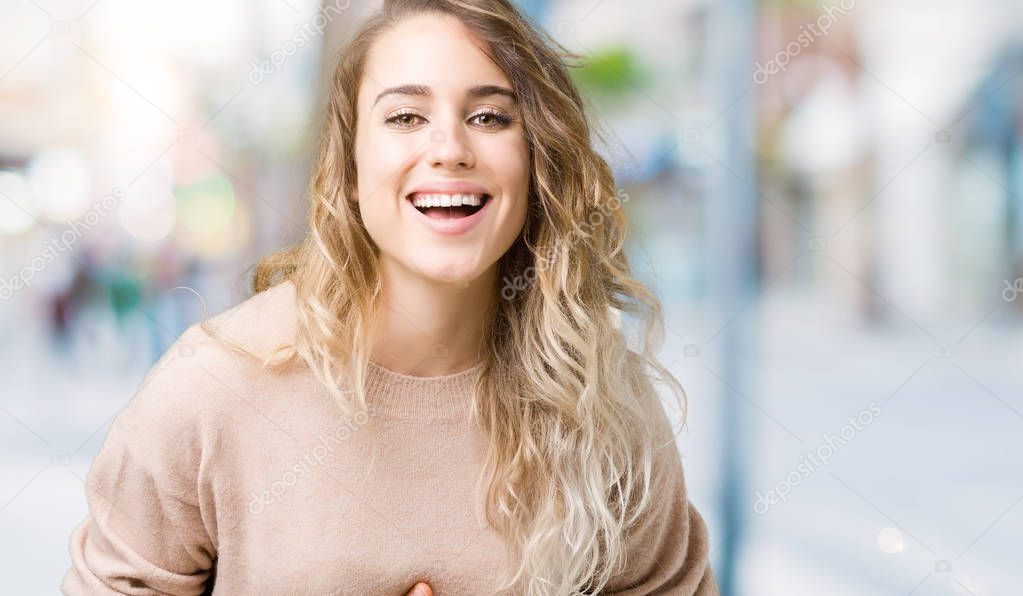 Beautiful young blonde woman wearing sweatershirt over isolated background Smiling and laughing hard out loud because funny crazy joke. Happy expression.