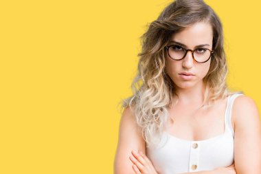 İzole arka plan şüpheci ve çapraz kolları olan yüzündeki gergin, onaylamayan ifade gözlüklü güzel sarışın genç kadın. Negatif kişi.