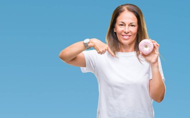 Orta yaş İspanyol kadın sürpriz yüz işaret parmağı kendini izole arka plan üzerinde pembe çörek yeme