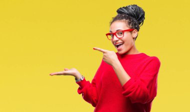 Genç örgülü kazak ve gözlük hayrete ve el ile sunulması ve parmak ile işaret ederken kameraya gülümseyen izole arka plan üzerinde giyen saç Afro-Amerikan Kız.