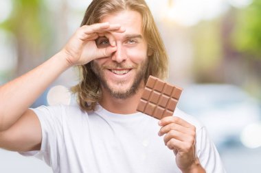 Uzun saç beslenme ile yakışıklı delikanlı ile mutlu yüz el parmaklarının arasından seyir göz üzerinde ok işaretiyle yapıyor gülümseyen izole arka plan üzerinde çikolata bar