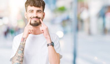 Beyaz t-shirt üzerinde izole giyen genç yakışıklı adam arka plan gülen açık ağız ile parmak işaret ve neşeli gülümseme zorlamadan