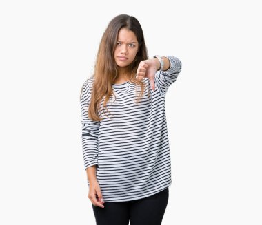 Mutsuz ve kızgın ret gösterilen ve başparmak aşağı hareketi ile negatif seyir izole arka plan üzerinde çizgili süveter giyen genç güzel esmer kadın. Kötü ifade.