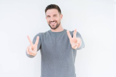 Zafer işareti yapıyor parmak gösterilen kamera seyir gülümseyen izole arka plan üzerinde rahat kazak giyen genç yakışıklı adam. İki numaralı.