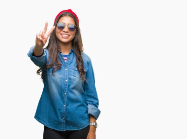 Genç güzel Arap kadın mutlu yüz zafer işareti yaparken kameraya göz kırpıyor ile gülümseyen izole arka plan üzerinde güneş gözlüğü takıyor. İki numaralı.