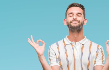 Yakışıklı delikanlı izole arka plan üzerinde dinlenmek ve gülümseyen gözlerle parmak ile meditasyon jest yapıyor kapalı. Yoga kavramı.