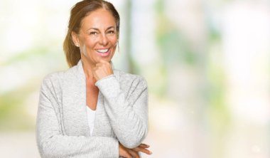 Emin çapraz kollar ve çeneme kaldırdı el ile gülümseme ile kameraya bakarak izole arka plan üzerinde kış kazak giyen güzel orta yaş yetişkin kadın. Pozitif düşünce.