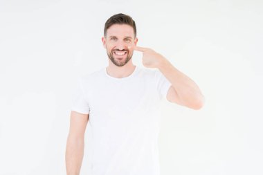 Casual beyaz t-shirt üzerinde izole giyen genç yakışıklı adam arka plan işaretçi el parmak yüz ve burun, neşeli gülümseyen