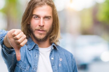 Mutsuz ve kızgın ret gösterilen ve başparmak aşağı hareketi ile negatif seyir izole arka plan üzerinde uzun saçlı Genç yakışıklı adam. Kötü ifade.