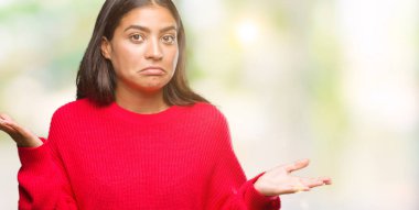 İzole arka plan clueless ve şaşkın bir ifadeyle kollar ve eller kaldırdı üzerinde kış kazak giyen genç güzel Arap kadın. Şüphe kavramı.