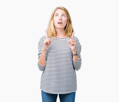 İzole arka plan üzerinde çizgili süveter giyen güzel genç kadın hayrete ve yukarıya bakıyor ve parmakları ile işaret ve silah kaldırdı şaşırttı.