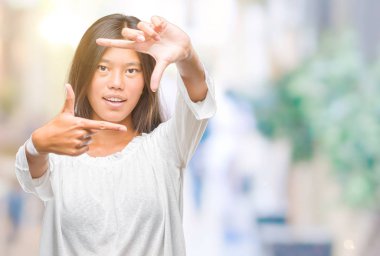 Genç Asyalı kadın elle yapma çerçeve ve parmakları ile mutlu yüz gülümseyen izole arka plan üzerinde. Yaratıcılık ve Fotoğrafçılık kavramı.