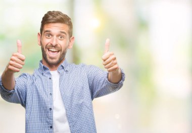 El ile pozitif jest yapıyor onaylama izole arka plan üzerinde beyaz t-shirt giyen genç yakışıklı adam başparmak gülümseyen ve başarı için mutlu. Kamera, kazanan jest arıyorsunuz.