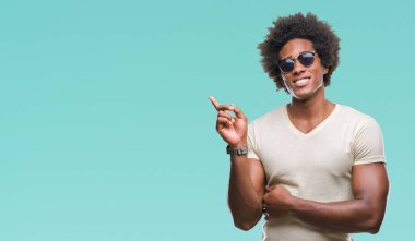Kameraya bakarak yan el ve parmak ile işaret Afro Amerikalı adam yüzünde kocaman bir gülümseme ile izole arka plan üzerinde güneş gözlüğü takıyor.